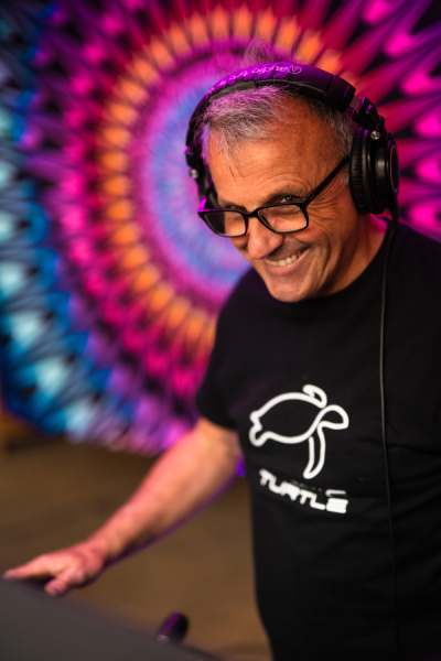 Cosmic Turtle DJing with a luminous mandala in the background